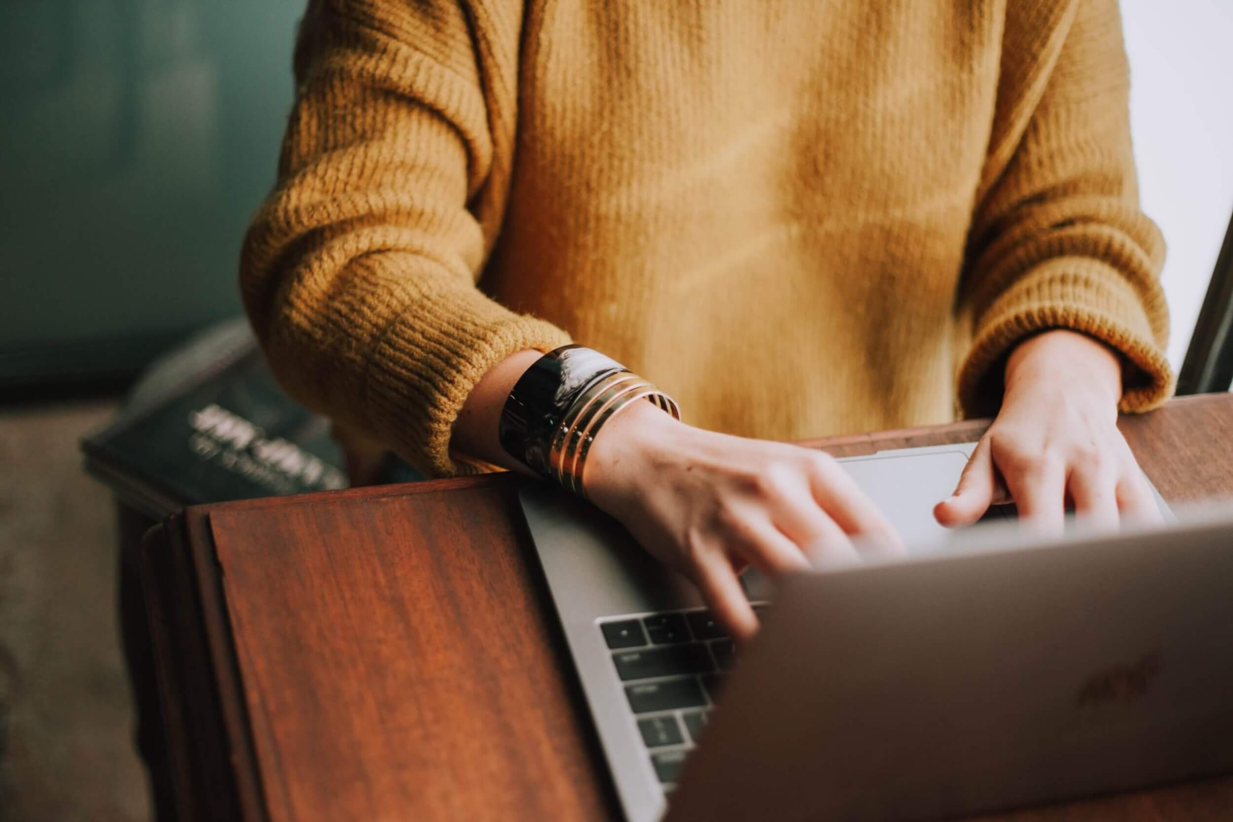 hands-with-cracelets-typing-on-laptop-in-jumper